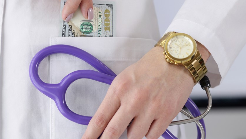 Close-up of woman doctor carry stethoscope tool and show piece of banknote in pocket. Pay to get qualified advice. Corruption in medicine, health concept