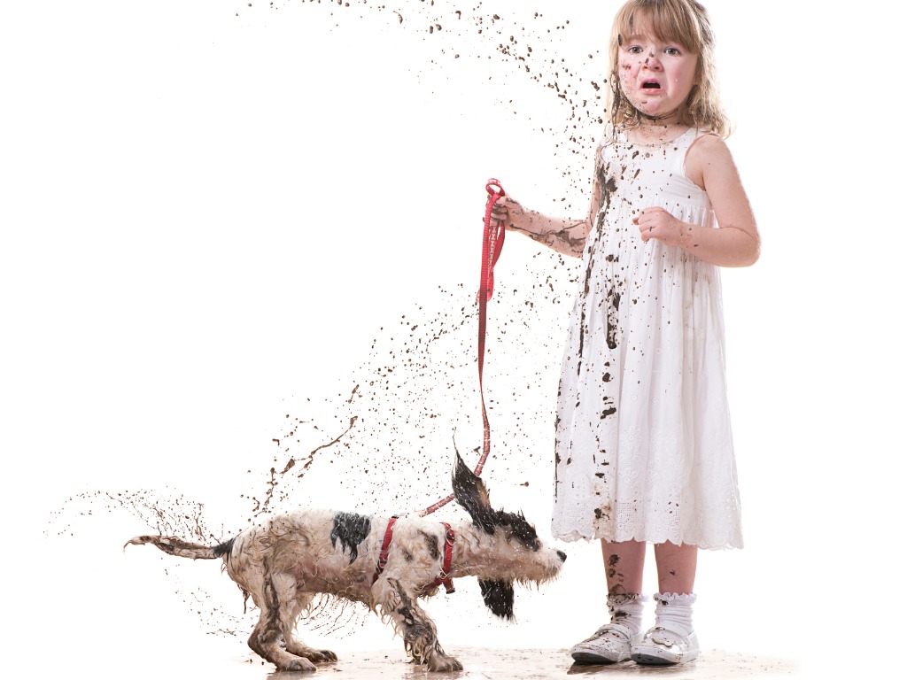 Shot of a little girl holding a leashed dog which is splashing the mud
